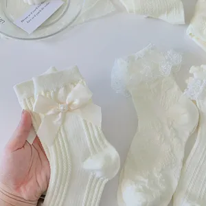 Gros plan de chaussettes mi-hautes Lolita blanches en dentelle avec nœud satiné et perle.