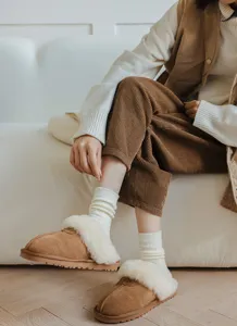 Detail shot of cozy white ribbed stacking socks styled with brown corduroy pants and slippers.