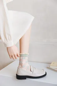 Close-up view of sheer mesh socks featuring blue clouds pattern and green ruffled cuffs.