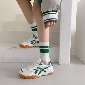 Detail shot of white and green striped tube socks paired with stylish sneakers on stairs.