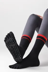 Close-up detail of black five-toe yoga socks with anti-slip grip dots and red stripe cuffs.