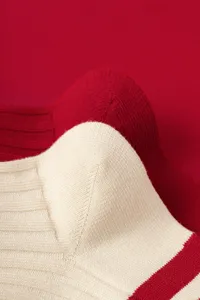 Close-up detail of red and beige knit mid-tube socks, showcasing fine ribbed texture.