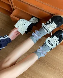 Close-up detail of grey polka dot mid-tube socks with cute lace bows and ruffles worn with sneakers.