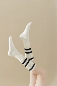 Close-up detail shot of white slouch socks with black double stripes, soft knit texture.