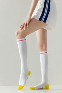 Detail view of women athletic knee-high socks in white with pink stripes and yellow toe accents.