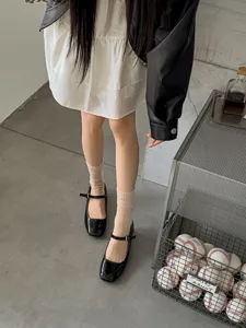 Sheer thin white stacking socks paired with fashionable black square toe Mary Jane shoes.