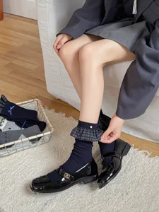 Close-up detail of dark blue ruffle socks with pearl charm and black Mary Jane shoes.