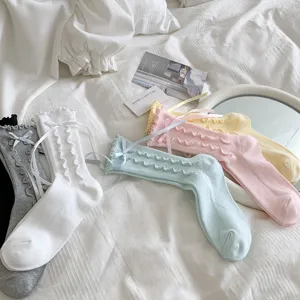 Detailed close-up of sweet ruffle bow mid-tube socks displayed on clean white bedding.