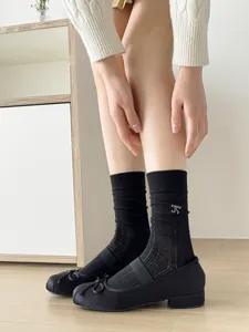 Close-up view of black mesh mid-calf slouch socks featuring delicate bow embroidery detail.