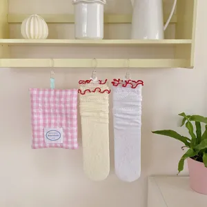 Close-up detail of sweet lace ruffle slouch socks and checkered pouch hanging on wooden shelf.