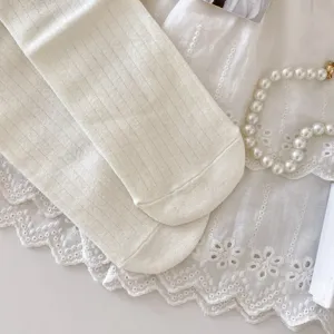 Close-up detail of cute white ribbed mid-tube socks with delicate lace fabric and pearl prop.