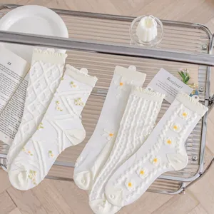 Nahaufnahme von weißen, transparenten Feinstrümpfen mit filigranen Blumen und Rüschenbündchen.
