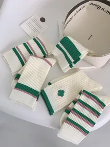 Green striped mid-tube socks detail view with cute clover embroidery and soft knit fabric.
