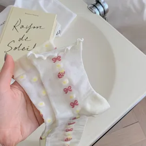 Close-up detail of cute white mid-calf socks featuring sweet bow and strawberry prints.