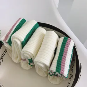 Close-up detail of folded white crew socks with green and pink stripes, soft knit fabric.