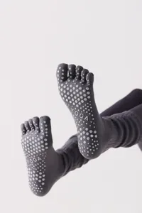 Primo piano dettagliato di calze da yoga grigie a cinque dita con pallini antiscivolo e design alto.