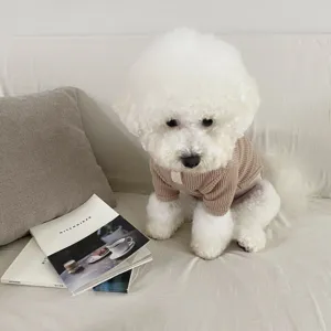 Detail shot of a brown waffle-knit pet sweater worn by a cute white Bichon dog on a cozy sofa.