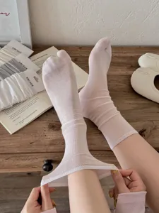 Close-up of thin solid split-toe slouchy socks worn on feet with rustic wooden tabletop background detail.