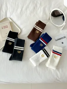 Detailed view of preppy style knee high socks with stripe details and embroidered crest emblem.