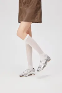 Close-up detail of white lace mesh knee-high socks worn with silver Mary Jane shoes.