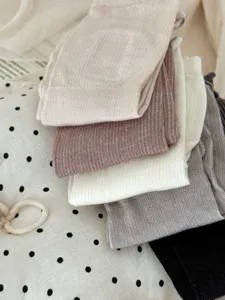 Close-up detail shot of stacked solid color silk mid-tube socks in various shades.