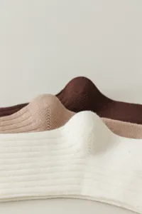 Close-up detail van gebreide lange sokken in wit, kameel en donkerbruin met fijne ribtextuur.