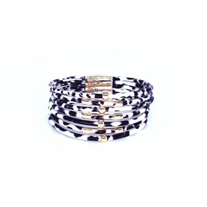 Primer plano de la pulsera de cuero con estampado de leopardo en blanco y negro y tubos dorados.