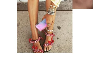 Vista detallada de sandalias rojas con estampado bandana y pulseras superpuestas en la pierna.