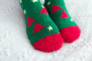 Close-up detail shot of plush Christmas fuzzy socks with festive tree patterns on white knit.