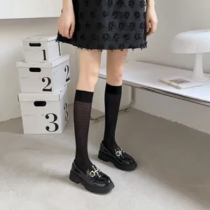 Detail shot of sheer black knee high socks worn with leather loafers for women summer style.