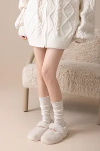 Close-up detail of cozy wool knit slouchy socks and fuzzy slippers in a warm styled room.