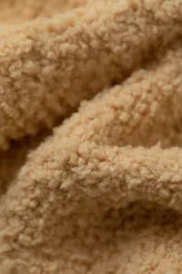 Primer plano de textura de tejido polar coral beige suave, detalle de material felpa invierno.