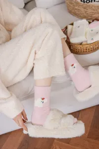 Détail de chaussettes douillettes roses avec broderie d'ours et fraise pour un usage intérieur.