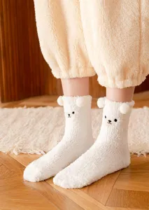 Close-up detail of fluffy white cute bear winter socks with plush ears and soft coral fleece.
