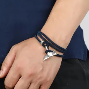 Detailed shot of a navy blue braided rope bracelet featuring a silver whale tail pendant.