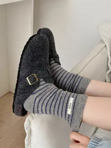 Close-up of cozy grey wool clogs paired with striped socks featuring a cute egg logo tag.