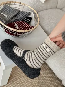 Close up view of striped wool mid-calf socks featuring a cute egg logo label and cozy home setup.