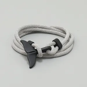 Detailansicht eines stilvollen grauen geflochtenen Armbands mit schwarzem Walflossen-Anhänger.