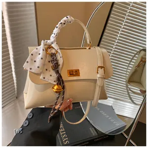 Detail shot of cream white top-handle bag with polka dot scarf ribbon and gold bell charm.