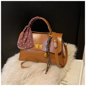 Detailed view of brown leather crossbody bag featuring polka dot ribbon and bell charm.