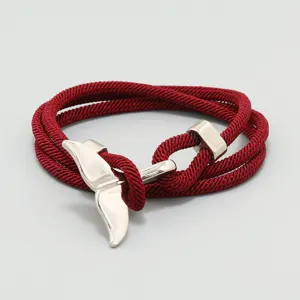 Detailansicht des roten geflochtenen Seilarmbands mit einem silbernen Walflossen-Anhänger.