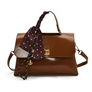 Stylish women's brown leather handbag with chic polka dot scarf and elegant metal lock.