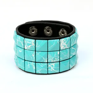 Pulsera de cuero ancha estilo punk con tres filas de tachuelas cuadradas turquesas y broches.