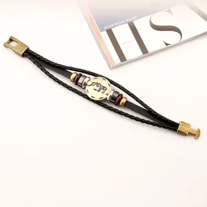 Primer plano detallado de una elegante pulsera de cuero trenzado multicapa con dijes del zodiaco.