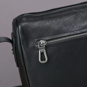 Close-up detail of black genuine cowhide men's shoulder bag with metallic zipper and texture.