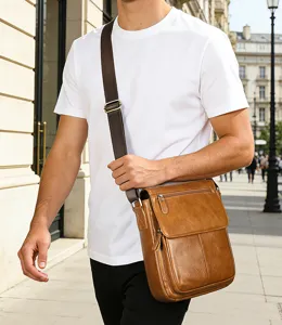 Gros plan extérieur du sac bandoulière en cuir marron porté par un modèle sur la rue.