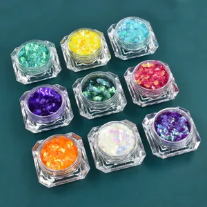 Dettaglio macro di otto vasetti contenenti scaglie di glitter iridescenti per unghie.