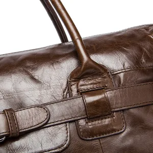 Gros plan de détail sur sac de voyage en cuir marron, montrant une texture rétro et des anses.