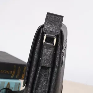 Black leather men shoulder bag detail close up showing metal hardware and pebble grain texture.