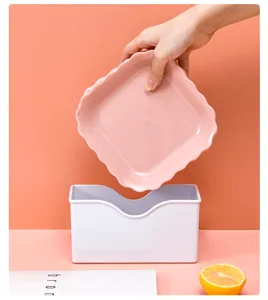 Detail view of a pink scalloped plastic serving plate and white storage box set for home.
